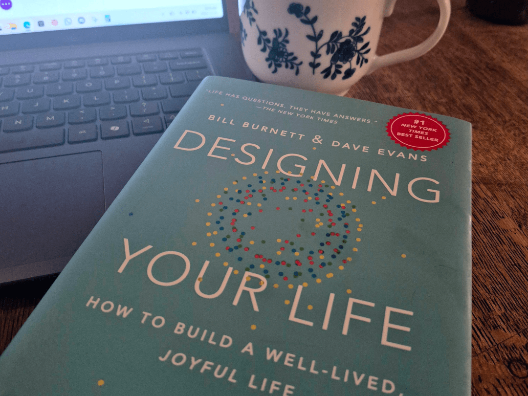 "Cover of 'Designing Your Life' by Bill Burnett and Dave Evans, with a cup and laptop in background, illustrating life design concepts."