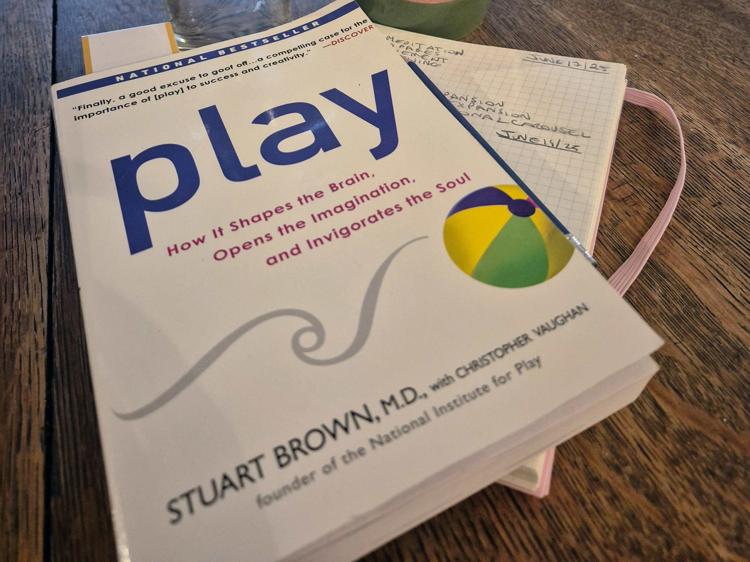 Book titled "Play" by Stuart Brown, emphasizing its impact on the brain and creativity, rests on a table next to a notebook with handwritten notes.